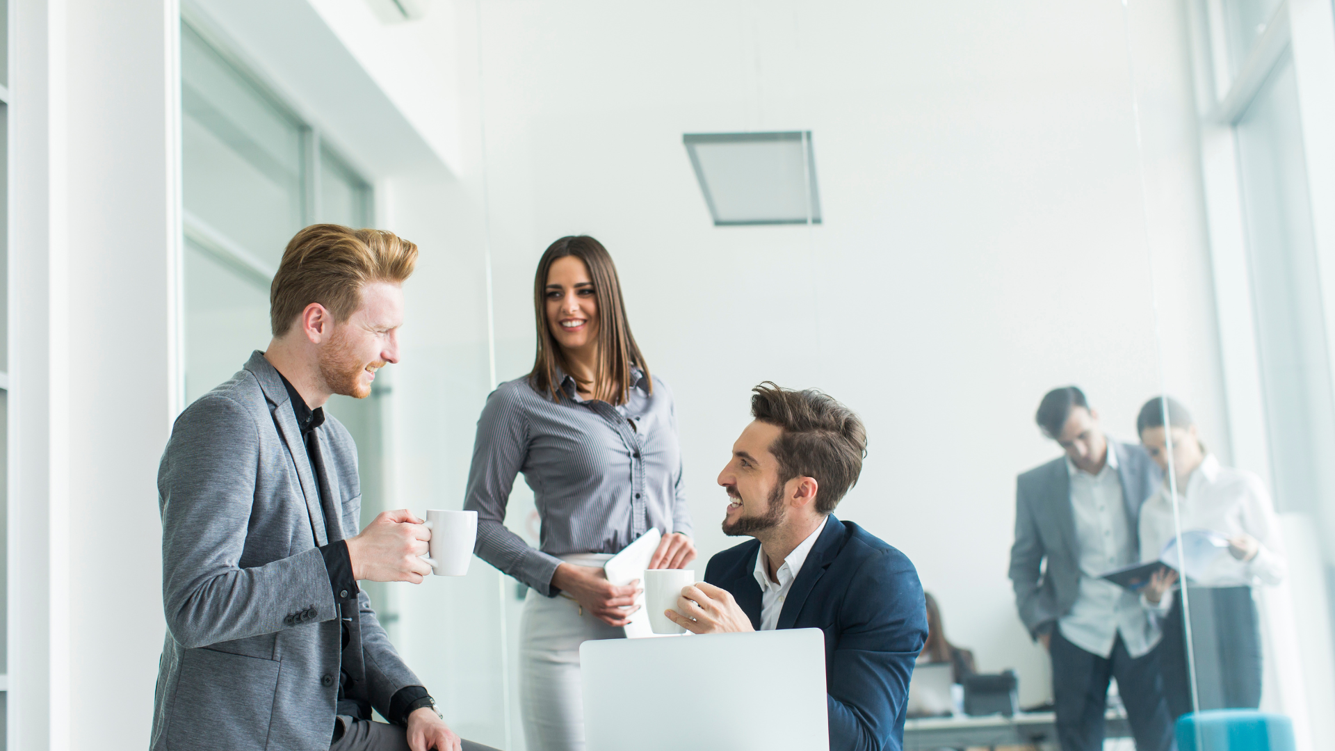 Office workers smiling and talking in a white office.
