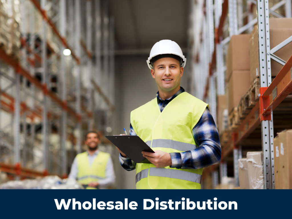 A warehouse worker holds a clipboard in front of a warehouse shelf.
