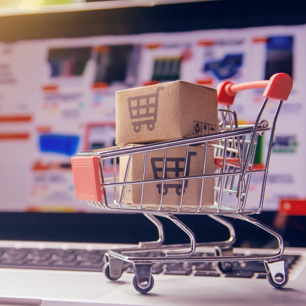 A shopping cart with boxes, in front of a laptop.