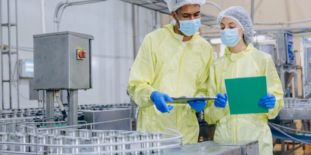 Food production workers in protective gear inspecting cans on a canning line